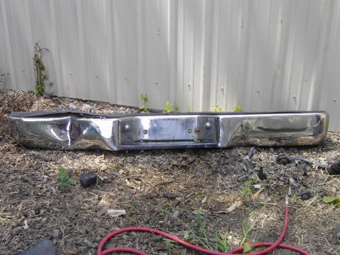1995 Jeep YJ - A damaged chrome rear bumper lies on the ground in front of a corrugated metal wall.