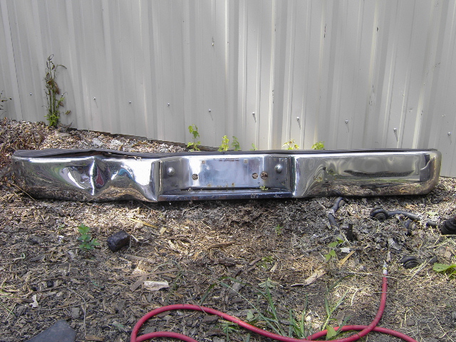 Chrome rear bumper with significant dents and damage, mounted on the ground