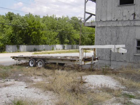1995 Jeep YJ - Flatbed trailer with a gooseneck hitch is parked outdoors next to a weathered building.