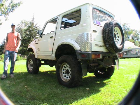 1977 Ford F-250 - A white Suzuki Samurai is shown from the rear with a person standing nearby on a grassy lawn.