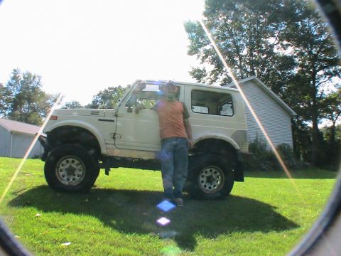 1977 Ford F-250 - A man stands next to a lifted Suzuki Samurai on a sunny day.