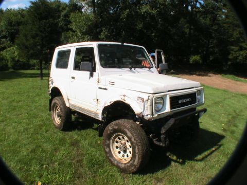 1977 Ford F-250 - A white Suzuki Samurai is parked on a grassy lawn with trees in the background.