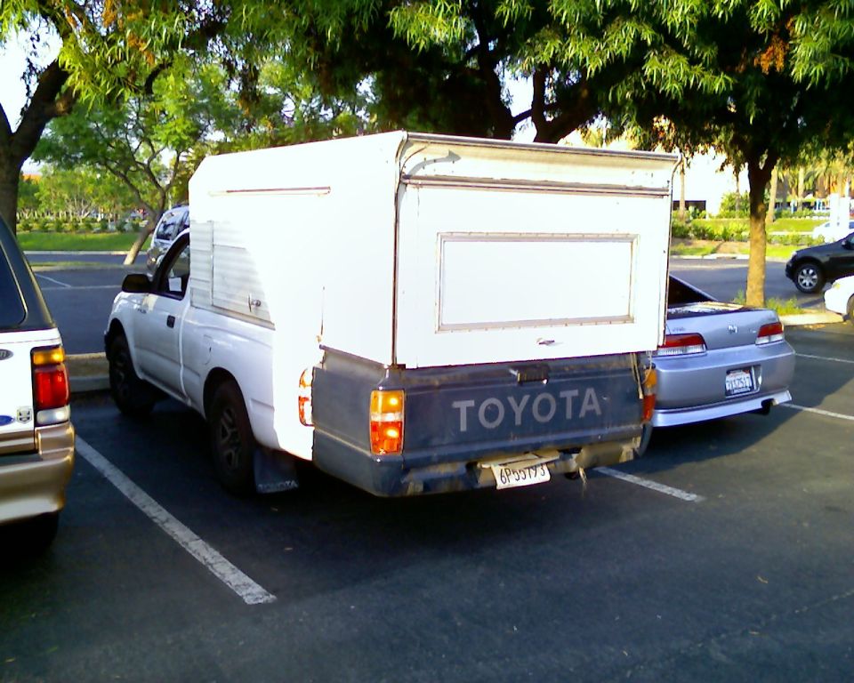 Rear view of white Toyota pickup with camper shell. License plate 6P3773