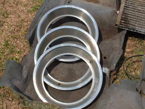 1966 Ford Ranchero - Three chrome wheel trim rings are laid out on a dark mat next to a car radiator.