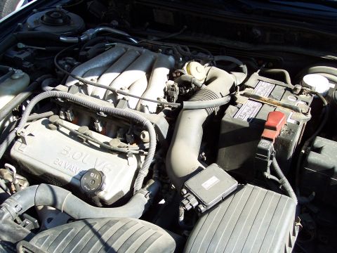 1995 Ford Probe - Close-up view of a car's engine bay, showing the "3.0L V6 24 VALVE" engine cover and battery.