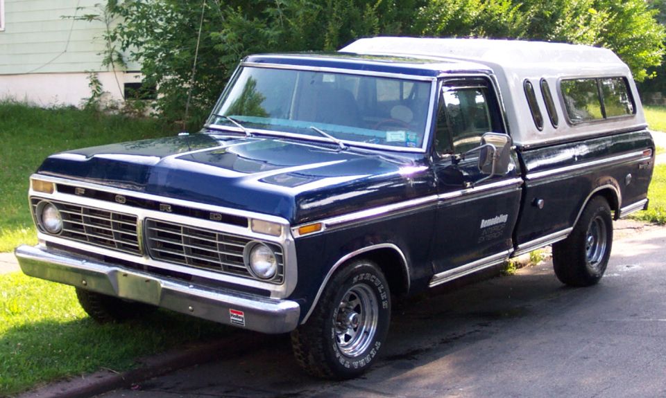 1975 Ford F-150 pickup truck, dark blue with silver camper shell, parked on a street