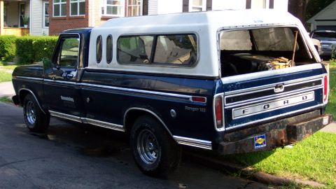 1975 Ford F-150 - This Ford pickup truck, identified as a 1975 model, is equipped with a camper shell and parked on a residential street.