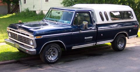 1975 Ford F-150 - A 1975 Ford F-150 pickup truck with a white camper shell is parked curbside.