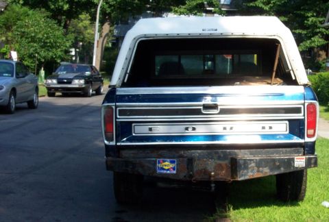 1975 Ford F-150 - This blue 1975 Ford F-150 pickup truck is seen from the rear, equipped with a white camper shell and a custom bumper.