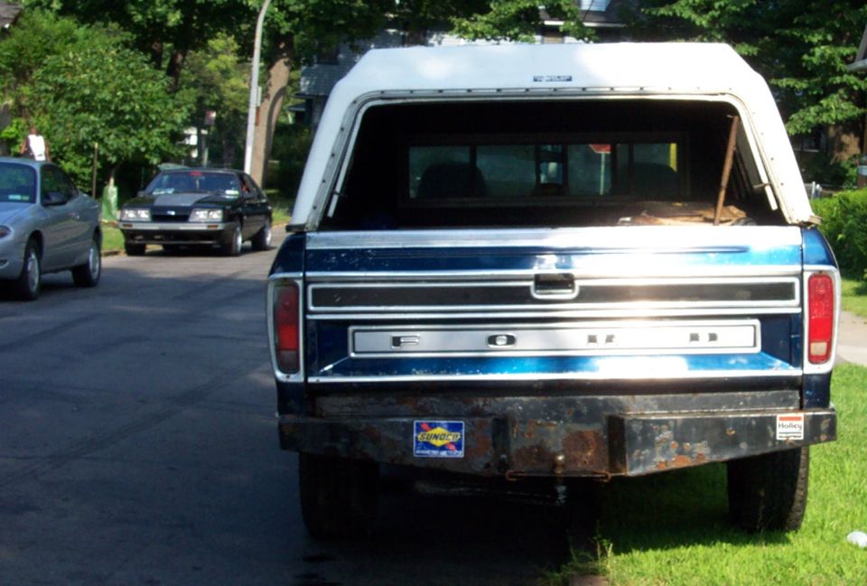 Rear view of blue 1975 Ford F-150 pickup with white camper shell and aftermarket bumper