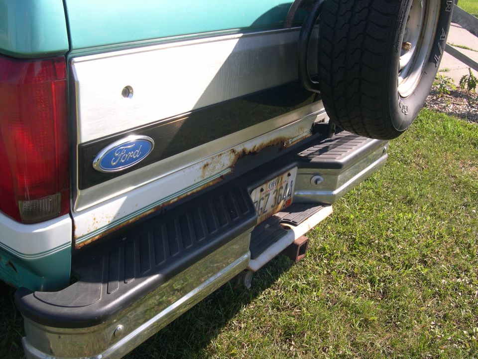 Rear of teal Ford Bronco with rusty tailgate, Ohio plate, chrome bumper and spare tire carrier