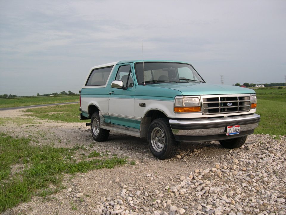 Two-tone teal and white Ford Bronco parked on gravel, front 3/4 view