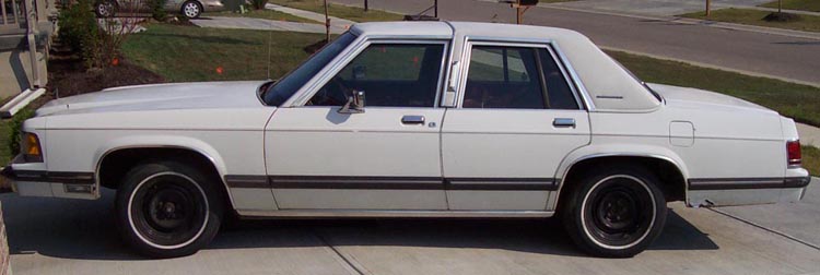 White sedan parked on driveway. Looks like an older model, maybe 1980s