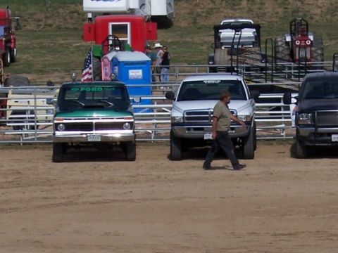 1972 Ford Ranchero - A man walks past a green Ford pickup truck and a white Dodge pickup truck at an outdoor event.