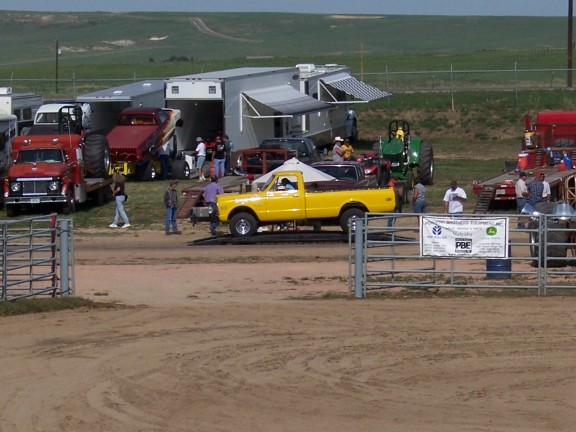 Yellow vintage Chevy pickup in the pits at an outdoor truck pull with haulers behind