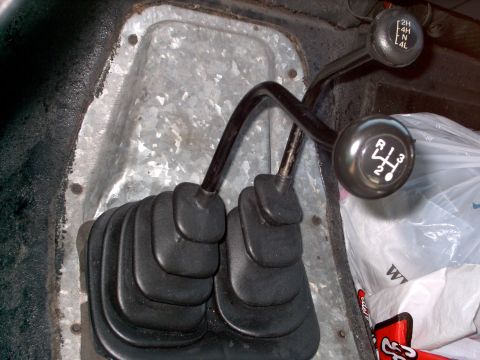 1982 Ford Bronco - Close-up of the manual transmission and transfer case levers inside a vehicle, showing the gear selection options.