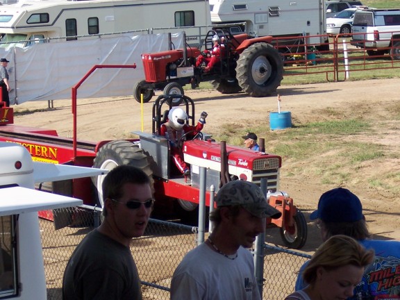 Red pulling tractor hitched to a sled at a dirt tractor pull with spectators