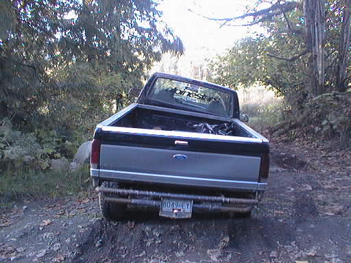 Rear view of black and silver Ford pickup with tailgate down on a muddy wooded trail