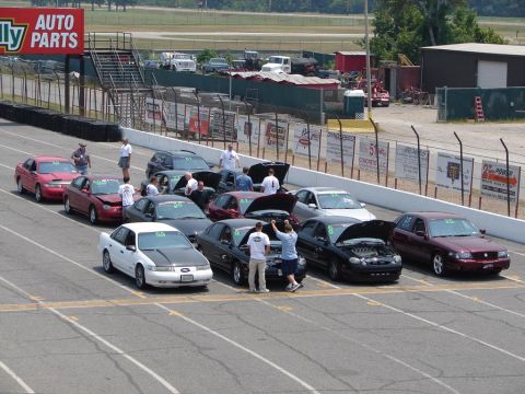 1992 Ford Taurus - A group of cars are staged on a drag strip, with several people attending to them.