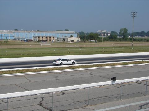 1992 Ford Taurus - A white 1992 Ford Taurus sedan is seen on a drag strip with industrial buildings in the background.