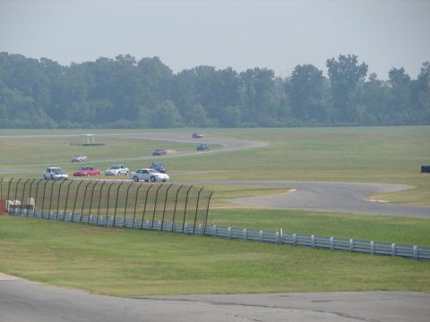 1992 Ford Taurus - Multiple vehicles compete on a winding race track under a hazy sky.