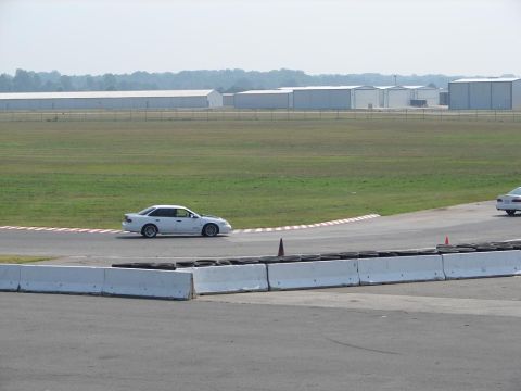 1992 Ford Taurus - A white 1992 Ford Taurus sedan navigates a turn on a race track, with another vehicle visible in the distance.