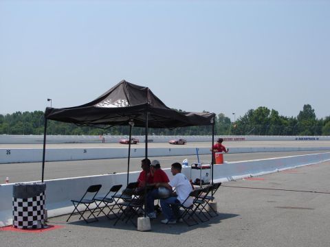 1992 Ford Taurus - A race track scene shows spectators under a tent while two cars are on the track in the distance.