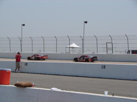1992 Ford Taurus - Stock cars compete on a sunny day at the racetrack, with spectators and barriers visible.