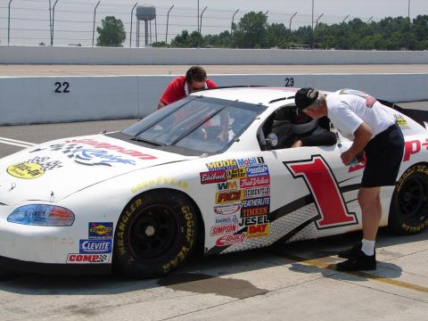 1992 Ford Taurus - Race car crew members inspect a stock car with numerous sponsor decals on the side.