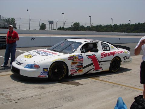 1992 Ford Taurus - A race car with various sponsor decals is parked on a track pit lane.