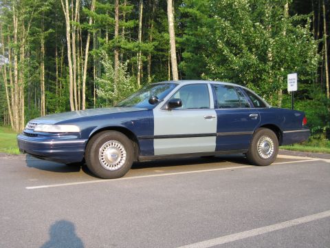 1991 Ford LTD Crown Victoria - A blue and gray sedan is parked in a lot with trees in the background.
