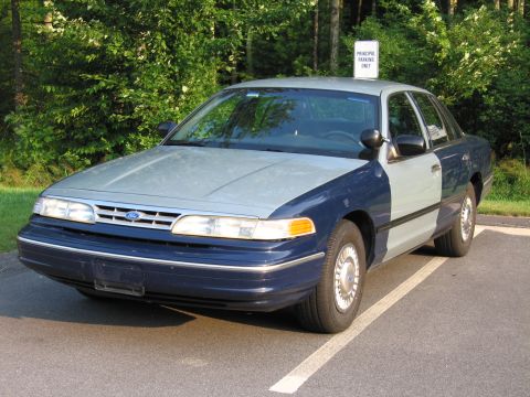 1991 Ford LTD Crown Victoria - A two-tone blue and silver 1992 Ford Crown Victoria sedan is parked in a lot with trees in the background.