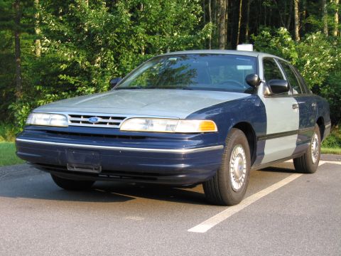 1991 Ford LTD Crown Victoria - A 1991 Ford Crown Victoria LTD with a two-tone paint job is parked in a lot with trees in the background.