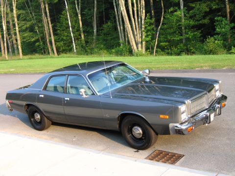 1991 Ford LTD Crown Victoria - A dark gray 1977 Dodge Monaco sedan is parked on the side of a road with trees in the background.