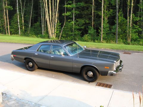 1991 Ford LTD Crown Victoria - A dark gray sedan is parked curbside with a wooded area in the background.