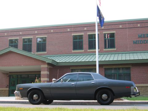 1991 Ford LTD Crown Victoria - This older model sedan, likely a police car, is parked outside a brick building with a flag pole.