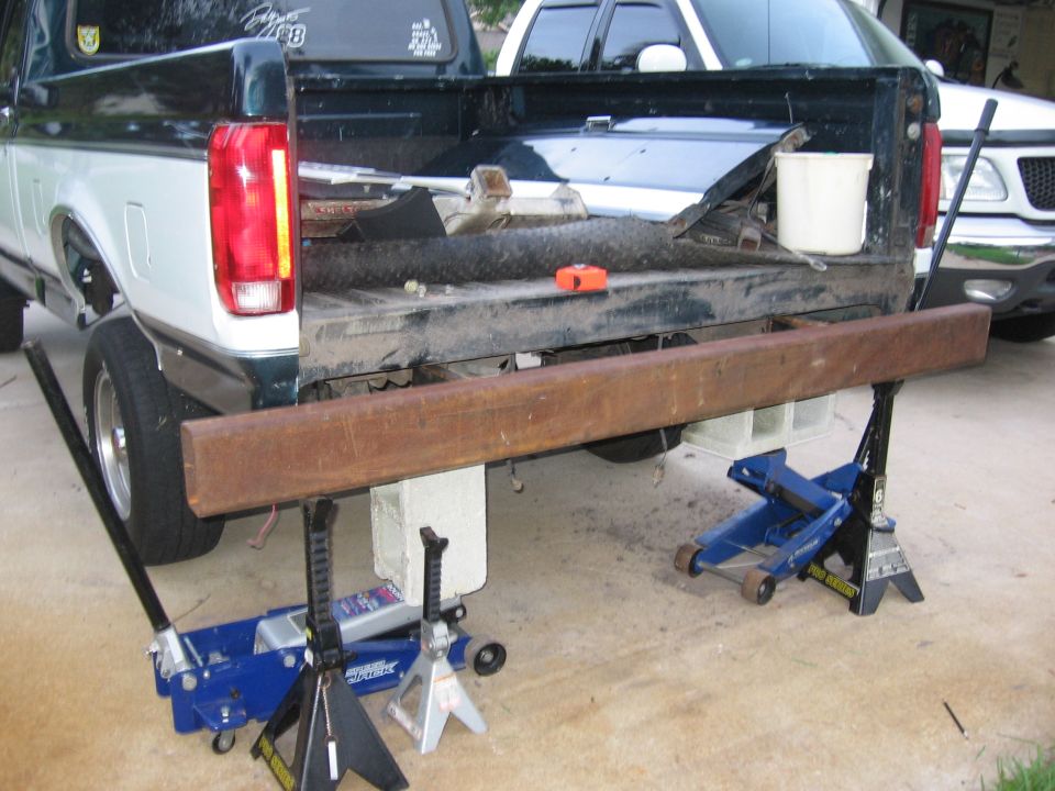 Truck bed with bumper removed, supported by jacks. Another truck is parked behind it