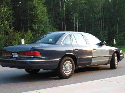 1991 Ford LTD Crown Victoria - A dark blue sedan with a mismatched grey front section is parked on the side of the road.