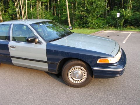 1991 Ford LTD Crown Victoria - A two-tone Ford Crown Victoria sedan is parked in a lot with trees in the background.
