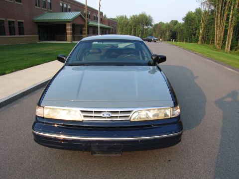 1991 Ford LTD Crown Victoria - A dark blue 1991 Ford Crown Victoria LTD sedan with a light blue hood is parked on a road in front of a brick building.