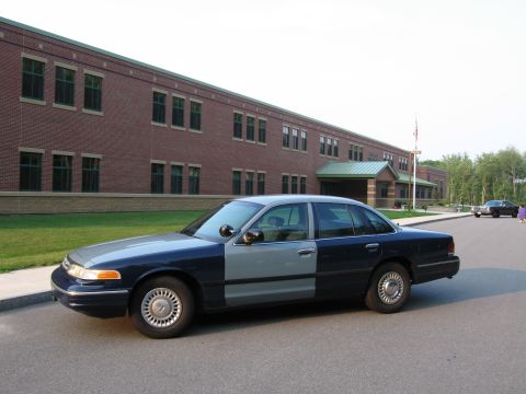 1991 Ford LTD Crown Victoria - A two-tone sedan is parked in front of a school building with another car visible in the background.