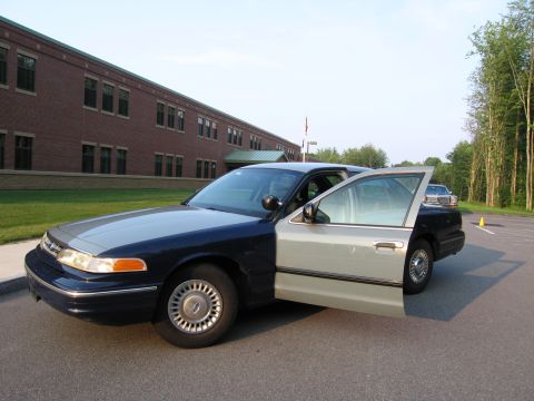 1991 Ford LTD Crown Victoria - A two-tone 1991 Ford Crown Victoria LTD is parked with its driver's side door ajar in front of a school building.