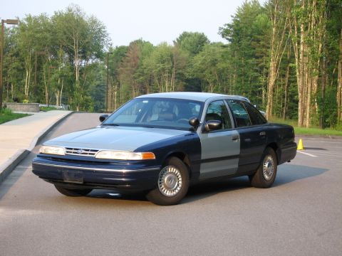 1991 Ford LTD Crown Victoria - A two-tone Ford Crown Victoria is parked on a paved surface with trees in the background.