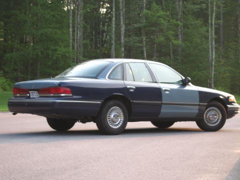 1991 Ford LTD Crown Victoria - A two-tone sedan, likely a 1992 model, is viewed from the rear quarter angle against a backdrop of trees.