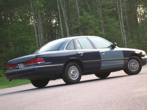 1991 Ford LTD Crown Victoria - A two-tone blue 1991 Ford Crown Victoria LTD is seen from the front three-quarter angle on a paved road with trees in the background.