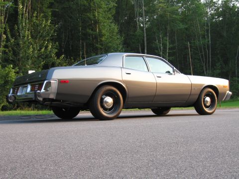 1991 Ford LTD Crown Victoria - Rear view of a 1977 Dodge Monaco sedan parked on a road with a wooded background.