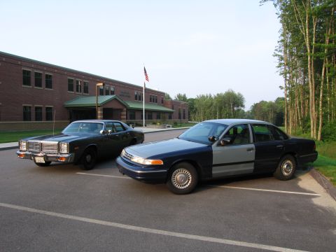 1991 Ford LTD Crown Victoria - A two-tone 1991 Ford Crown Victoria is parked in front of a brick building, with an older dark sedan to its left.