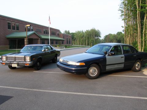 1991 Ford LTD Crown Victoria - Two sedans are parked in a lot in front of a school building.