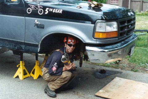 1995 Ford F-150 - A person works on the underside of a two-tone Ford F-150 truck supported by yellow jack stands.