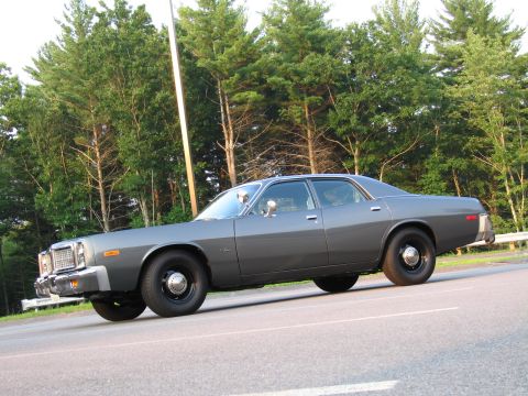 1991 Ford LTD Crown Victoria - This gray 1977 Dodge Monaco sedan is seen from the side, parked on a road with trees in the background.